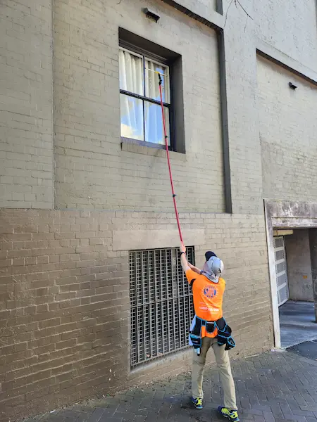 Window cleaner using a traditional extension pole and squeegee to clean second-storey windows from the ground